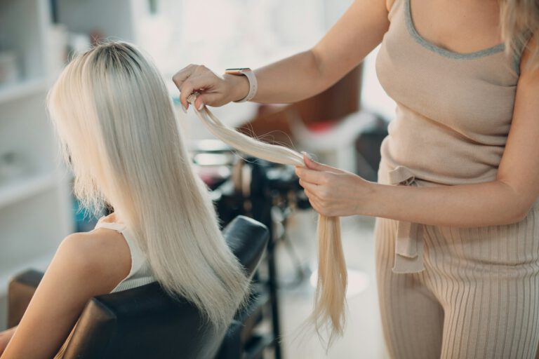 Hairdresser female making hair extensions to young woman with blonde hair in beauty salon.