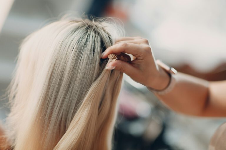 Hairdresser female making hair extensions to young woman with blonde hair in beauty salon.