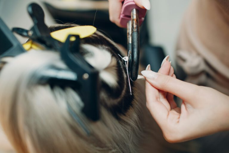 Hairdresser female making hair extensions to young woman with blonde hair in beauty salon.