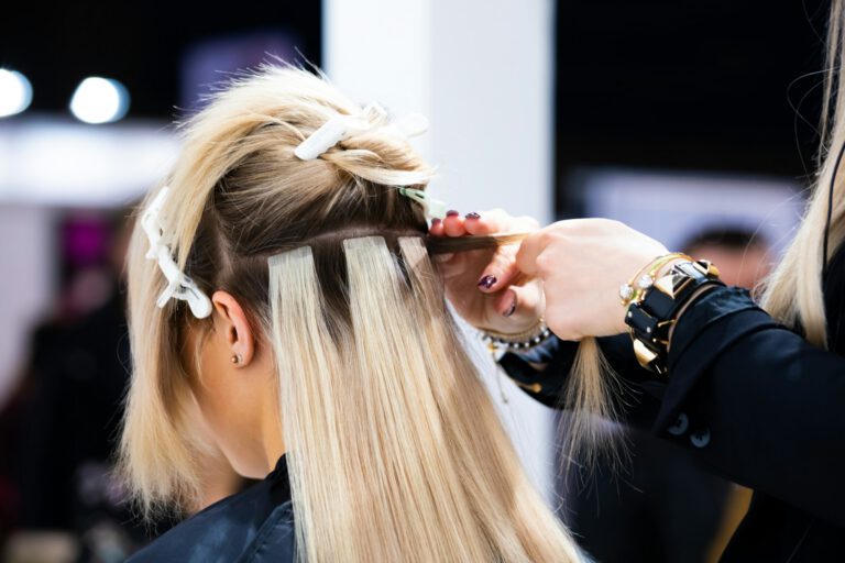 Professional hairdresser making hair extensions for blonde girl in a beauty salon